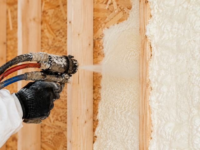 Close view of spray foam insulation being sprayed between wood studs