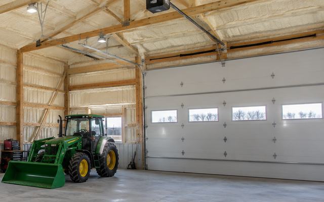 Tractor parked beside an overhead door in a farm building with spray foam insulation