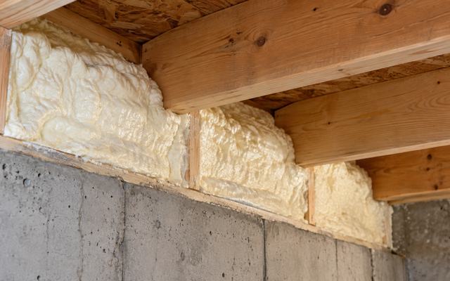 Closed-cell spray foam sealing a basement rim joist above a concrete foundation wall